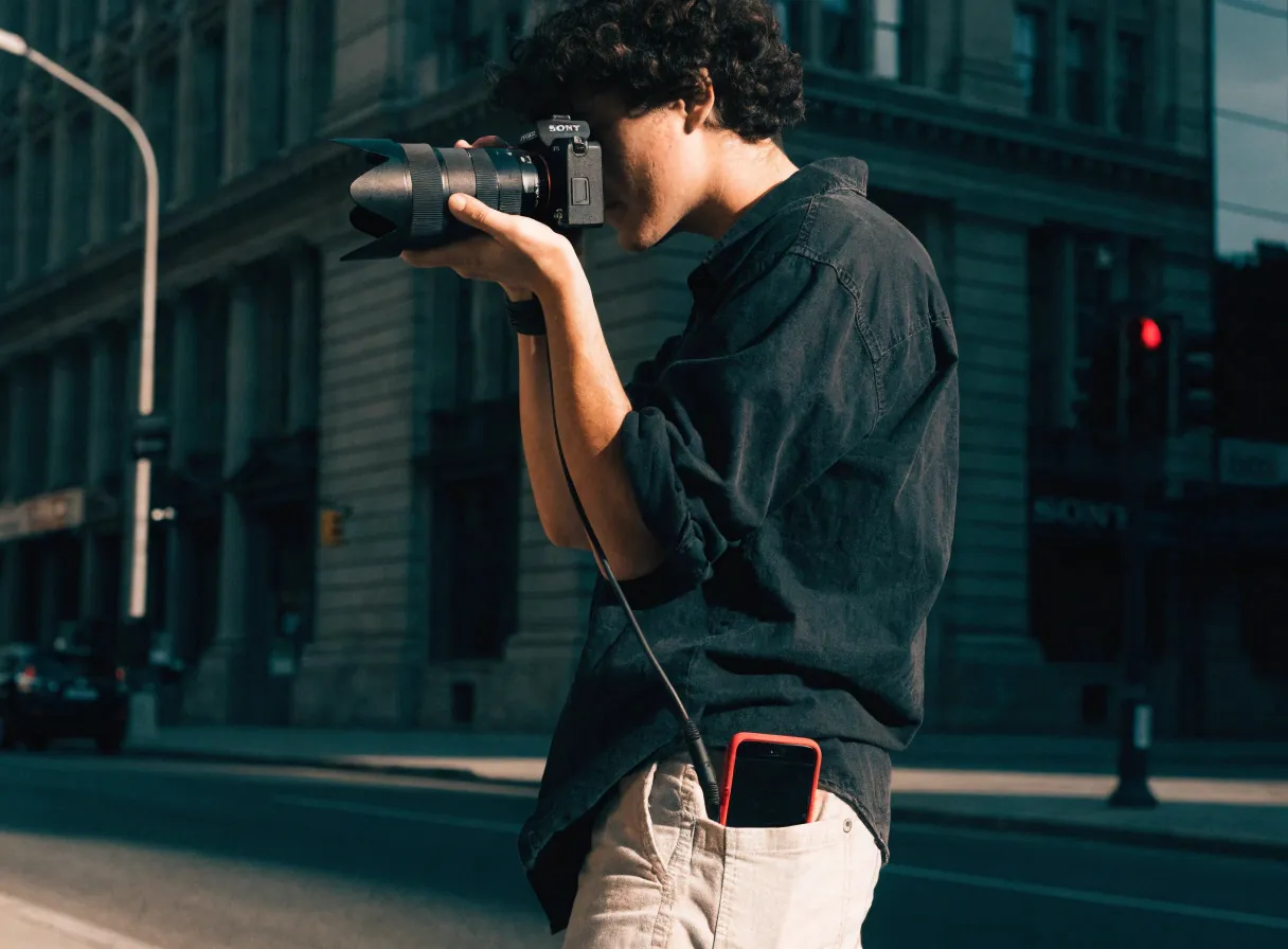 Fotografer memotret di jalan dengan kamera yang terhubung ke ponselnya.